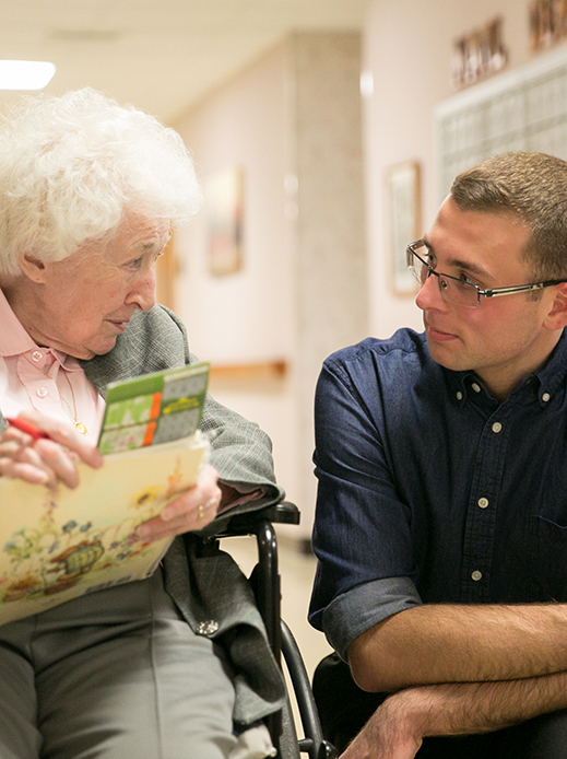 A person ministering to an elderly woman in a wheelchair.